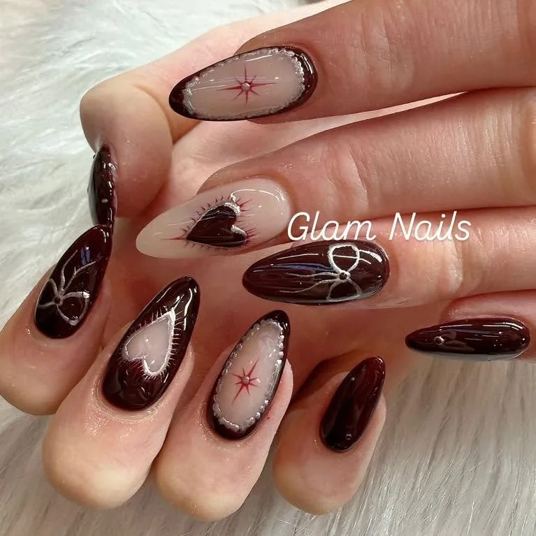 Dark burgundy almond nails with white and silver hearts, bows and compass-star art