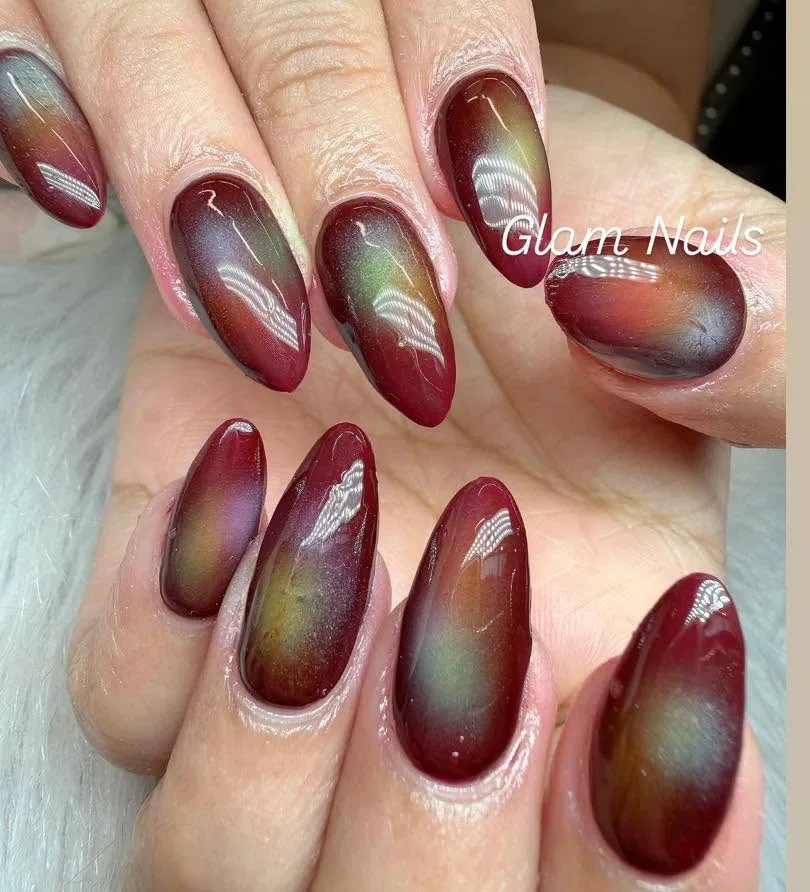 Oxblood magnetic cat-eye almond nails with green-gold aurora shimmer