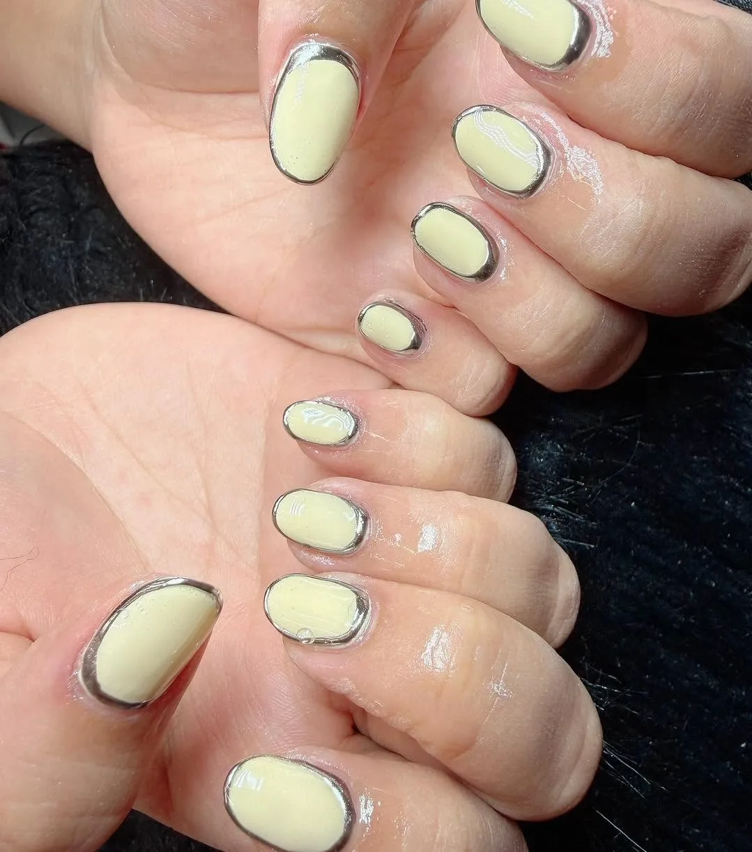 Pale butter-yellow short round nails with silver mirror-chrome outline