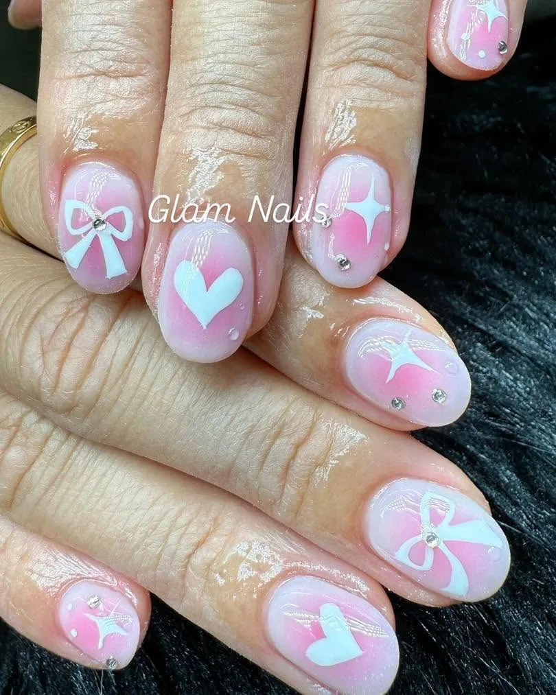 Short round nails in pink ombré with white bows, hearts, stars and rhinestones