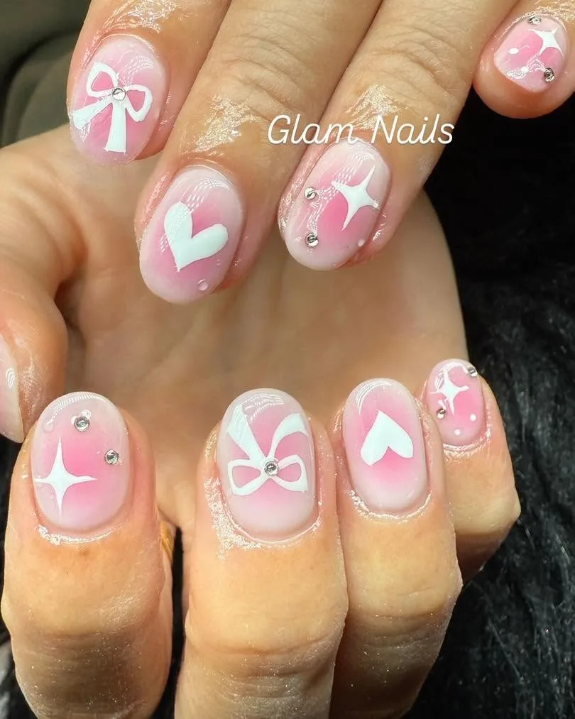 Short round nails in pink ombré with bows, hearts, sparkles and rhinestones